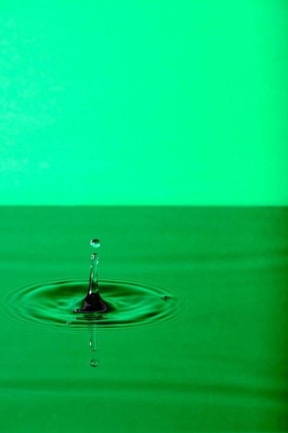 Splash drop of water with diverging water circles on green background