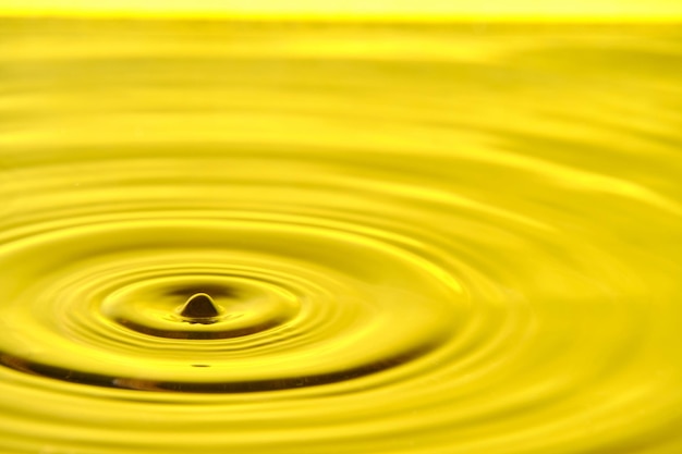 Splash drop of water with diverging water circles on yellow background