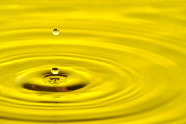 Goccia d'acqua spruzzata con cerchi d'acqua divergenti su sfondo giallo