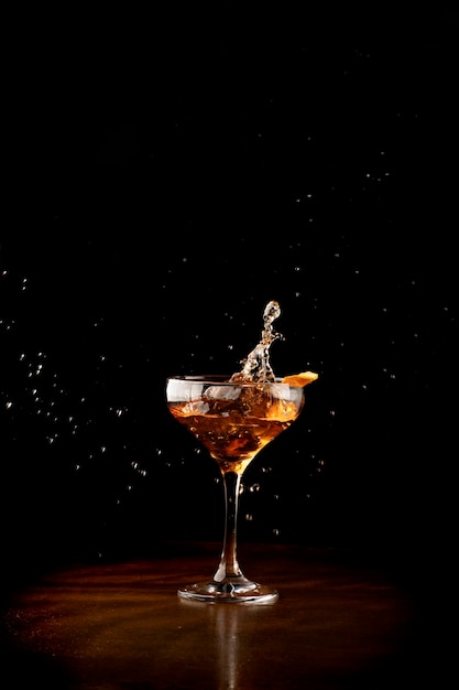 Splash in glass of bourbon whiskey cocktail with on wooden table and dark background