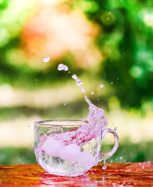 Splash van koel zoet water met ijsblokje in de transparante glazen beker in de tafel buiten in de zomerdag