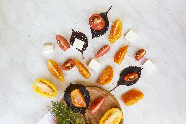 Splash van seizoensgebonden gezonde salade met rode oranje en gele tomaten basilicum dille feta kaas sesam op witte marmeren achtergrond close-up natuurlijke biologische voeding bovenaanzicht voedsel