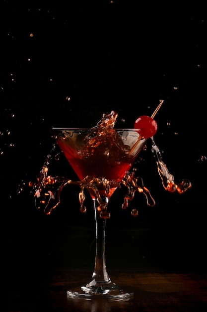 Splash with red drink in martini glass and cherry and dark background