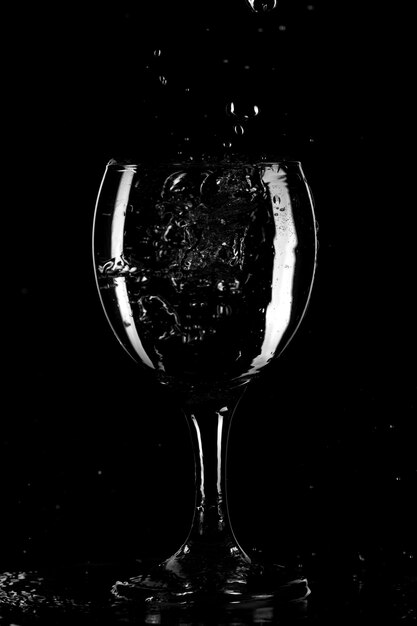 Splashes and drops of water in a glass are isolated on a black background. Blue water in a glass