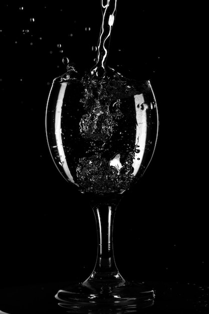 Splashes and drops of water in a glass are isolated on a black background. Blue water in a glass