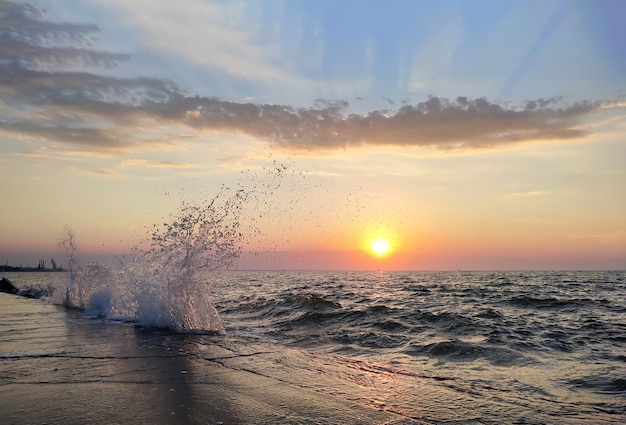 日没の自然の背景で海に波をはねかける
