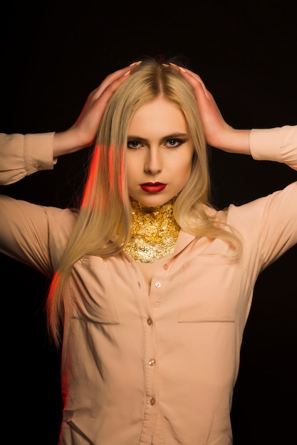 Splendid blonde model with long hair and gold foil on her neck posing at studio