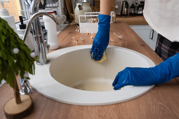 Spoelbak in de keuken schoonmaken voor de kerst- en nieuwjaarsvakantie Handschoenen en spons wasmiddel droog poeder inleveren Feestelijke inrichting in de witte keuken, gezellig interieur van het huis