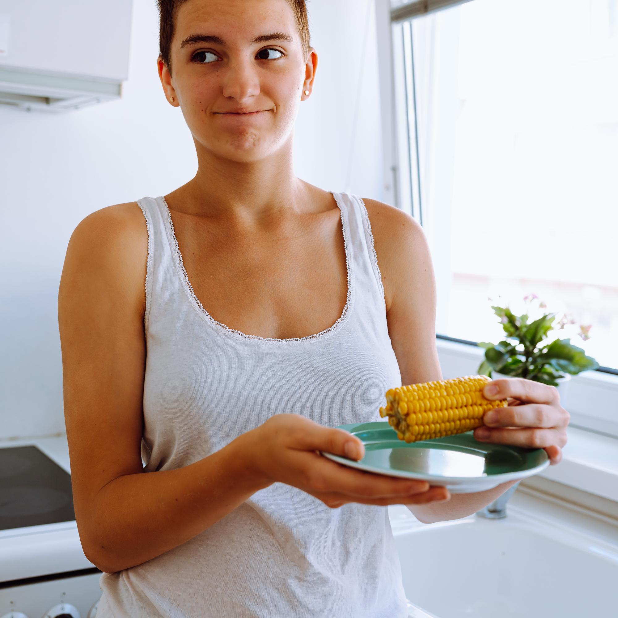 Spoiled bad food. teenage girl at home in kitchen holds plate of boiled corn, sour from long-term