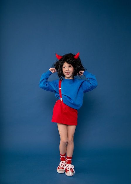 버릇없는 아이, 장난 꾸러기 소녀, 아이들의 변덕. 캐릭터를 보여주는 빨간 꼬마 도깨비 뿔이 발에 아름 다운 작은 소녀. 아동 위기 심리학 개념. 전체 길이 사진