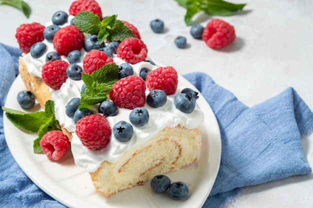 Foto sponge biscuit cake roll vulling slagroom en bessen versierd frambozen en bosbessen zomer voedsel concept