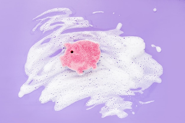 Photo sponge of cute pig shaped on soapy foam background. washing dishes concept. flat lay, top view.