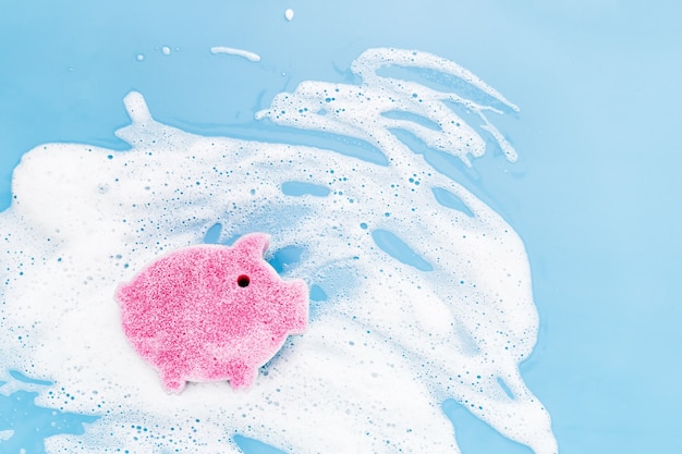 Sponge of cute pig shaped on soapy foam background. Washing dishes concept. Flat lay, Top view.