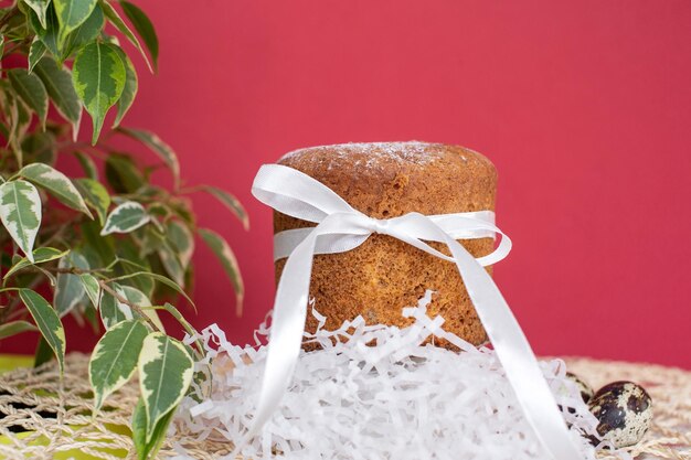 Sponge Easter cake with a white ribbon with quail eggs on a red background with a green plant
