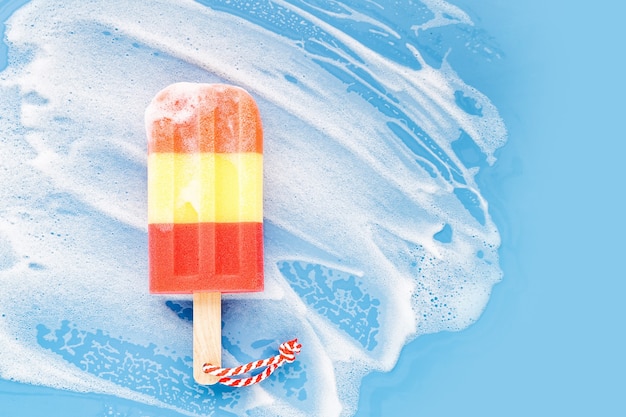 Sponge in the form of ice cream on soapy foam background. Washing dishes concept. Flat lay, Top view.