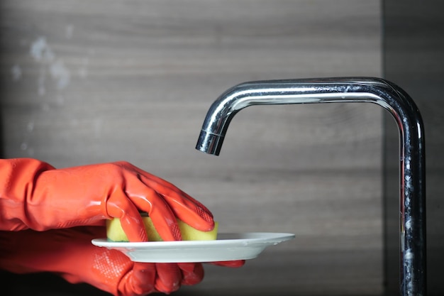 Sponge hand in red rubber gloves cleaning a plate with sponge