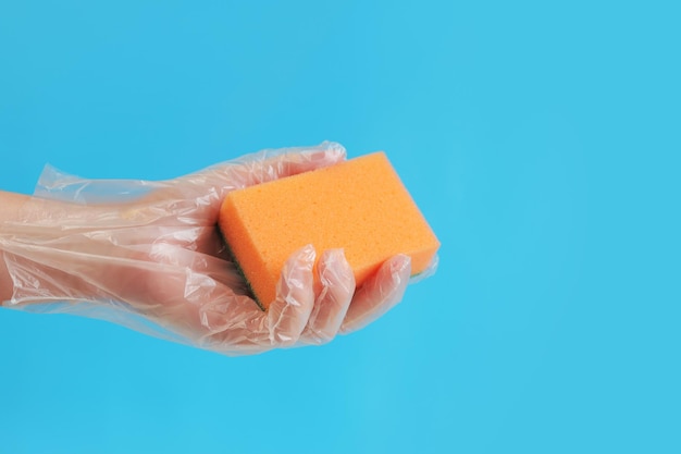 Sponge in hand wet cleaning of the room bright blue background A womans hand in a glove