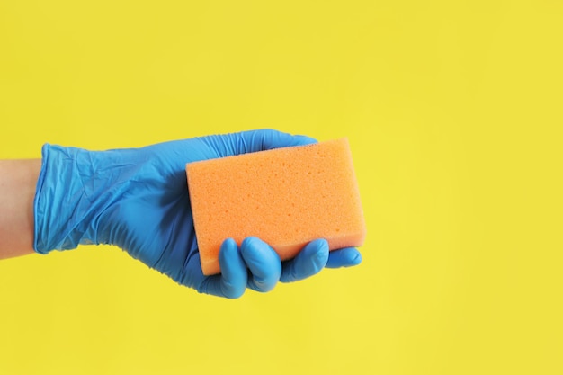 Sponge in hand wet cleaning of the room bright yellow background hand in a latex blue glove