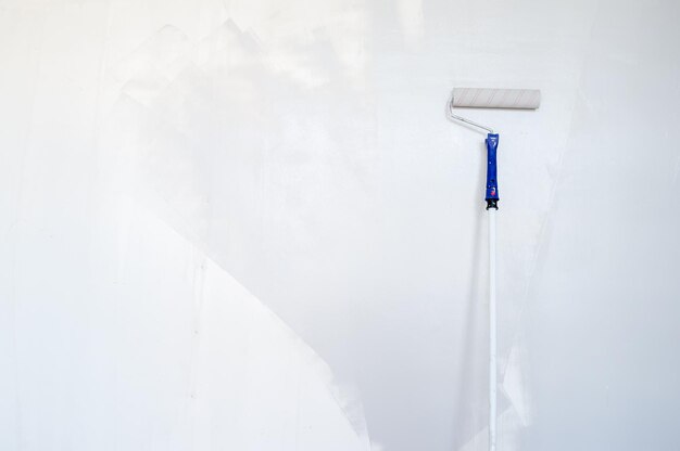 Photo sponge roller on a wooden stick repaints the wall gray. home renovation. copy space