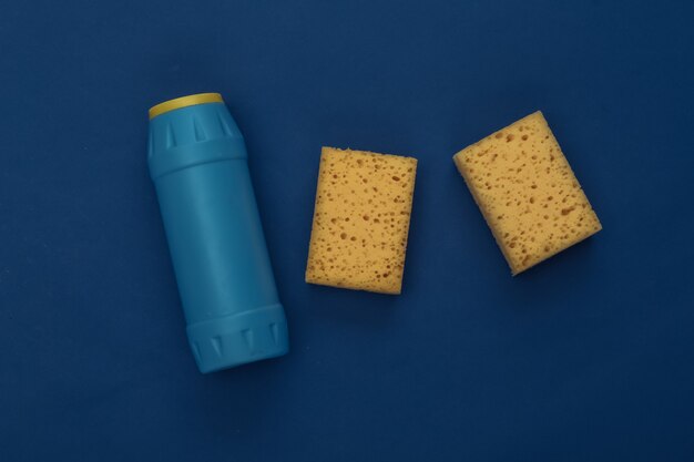 Sponges and bottle of detergent on classic blue background. Color 2020. House cleaning theme. Top view