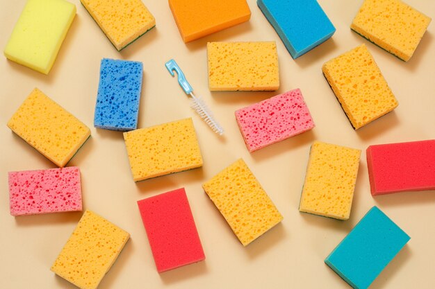 Sponges of different colors and a small brush on the beige background. Top view. Washing and cleaning set.