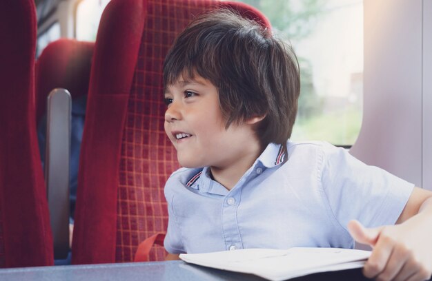 Spontaan schot opgewonden kind kijkt uit de trein met blij gezicht, schooljongen plezier maken reizen met de trein voor een dagtocht, schattige kleine jongen met lachende gezicht gelukkige tijd op zijn zomerkamp.