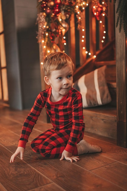 Spontane authentieke blij lachende kleine jongen in rode geruite pyjama die rondhangt bij lodge Xmas versierd