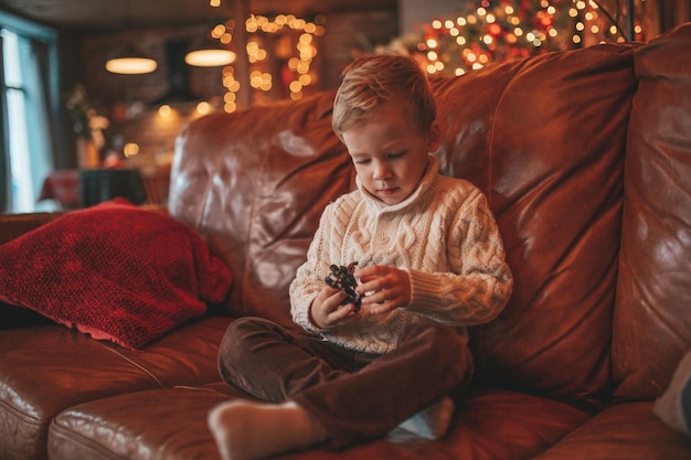 Spontane authentieke vrolijke kleine jongen in gebreide beige trui die aan het dollen is in lodge Xmas ingericht