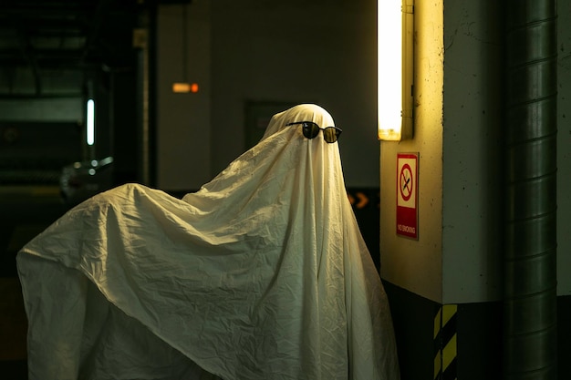 Призрачный призрак в простыне на подземной парковке смотрит на знак запрета на курение