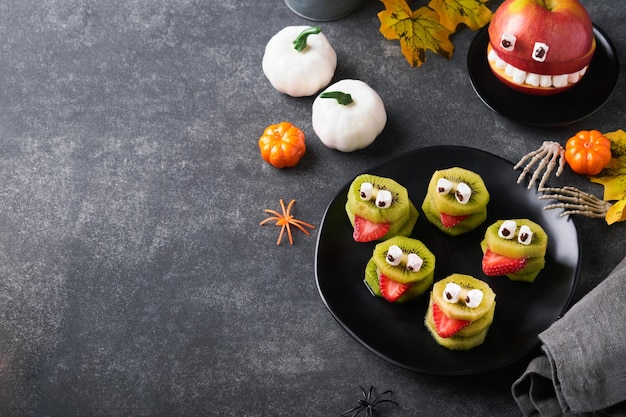 Spooky green kiwi monsters for Halloween Healthy Fruit Halloween Treats Halloween party kiwi strawberry apple and marshmallow monster on dark grey stone or concrete table background