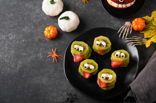 Spooky green kiwi monsters for Halloween Healthy Fruit Halloween Treats Halloween party kiwi strawberry apple and marshmallow monster on dark grey stone or concrete table background