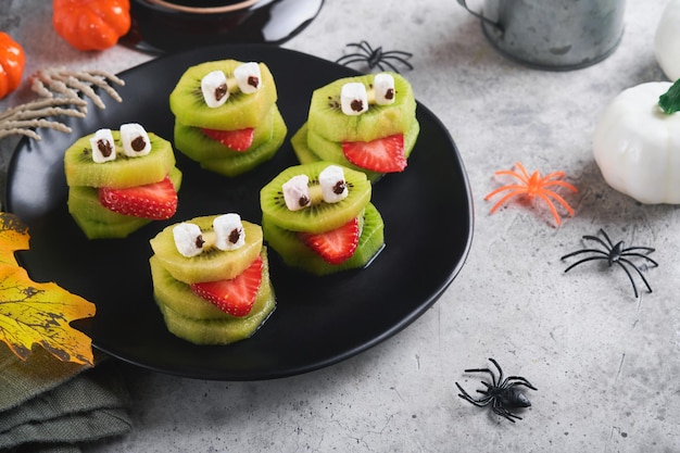 Spooky green kiwi monsters for Halloween Healthy Fruit Halloween Treats Halloween party kiwi strawberry apple and marshmallow monster on grey stone or concrete table background Selective focus