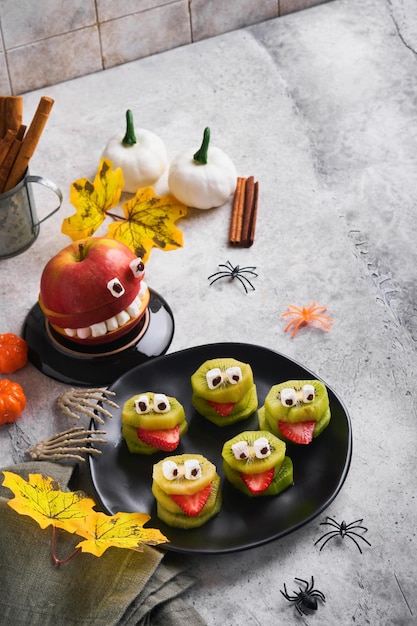 Spooky green kiwi monsters for Halloween Healthy Fruit Halloween Treats Halloween party kiwi strawberry apple and marshmallow monster on grey stone or concrete table background Selective focus