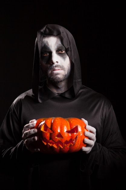 Spooky grim reaper tenendo una zucca su sfondo nero, vestito di halloween.