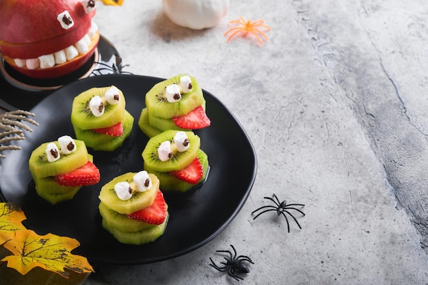 Spooky groene kiwi monsters voor Halloween gezond fruit Halloween behandelt Halloween party kiwi aardbei appel en marshmallow monster op grijze steen of betonnen tafel achtergrond Selectieve aandacht