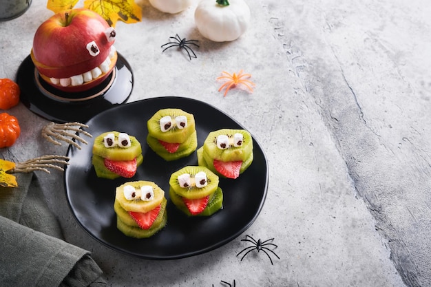 Spooky groene kiwi monsters voor halloween gezond fruit halloween behandelt halloween party kiwi aardbei appel en marshmallow monster op grijze steen of betonnen tafel achtergrond selectieve aandacht