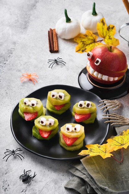 Spooky groene kiwi monsters voor halloween gezond fruit halloween behandelt halloween party kiwi aardbei appel en marshmallow monster op grijze steen of betonnen tafel achtergrond selectieve aandacht