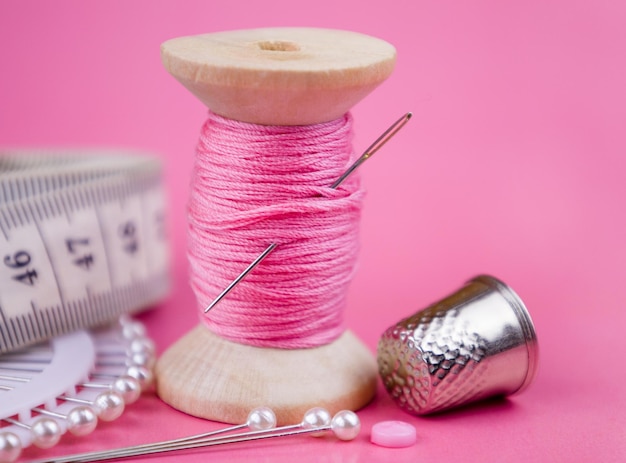 Premium Photo  A spool of pink thread a needle and a thimble on a pink  background