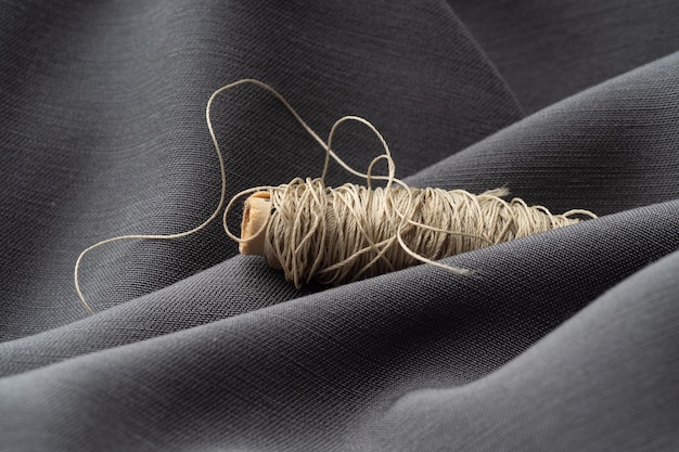 A spool with beige threads in a draped soft gray fabric closeup macro Atelier tailoring sewing background The texture of silk threads and satin fabric Fashion designer high fashion concept
