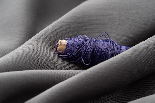 Una bobina con fili viola in un tessuto grigio morbido drappeggiato primo piano macro atelier sartoria sfondo cucito la trama di fili di seta e tessuto satinato concetto di alta moda stilista