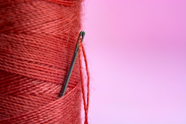 Spool with red thread and needle on pink