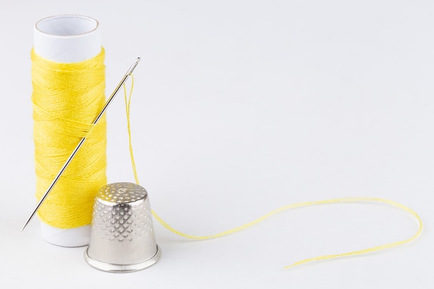 Photo spool of yellow threads and a needle on white background