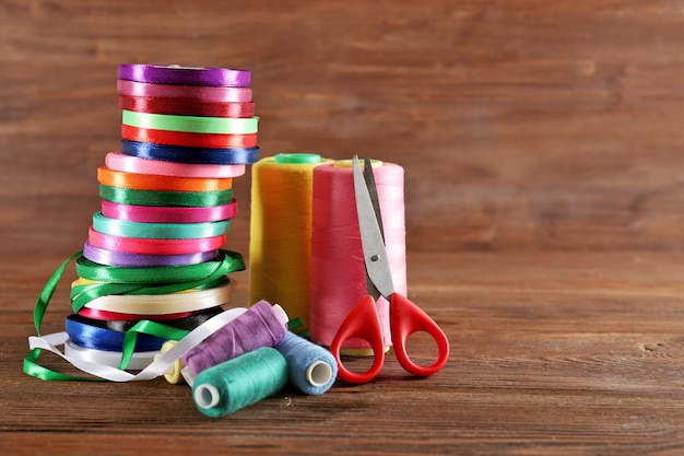 Spools of color ribbon with scissors thread on wooden background