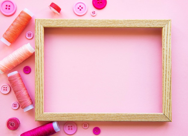 Photo spools of thread and buttons in pink tones on pink, flat lay