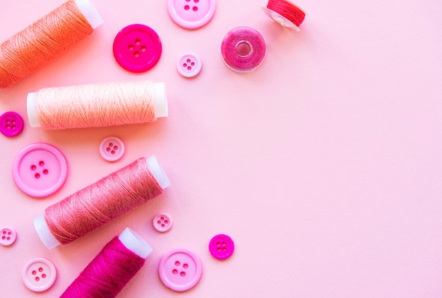 Spools of thread and buttons in pink tones on a pink surface