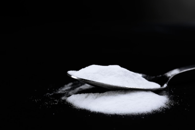 Spoon of baking soda on black background