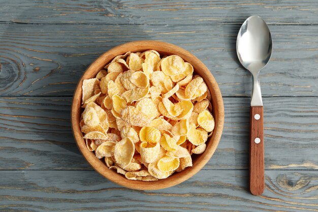 Spoon and bowl of cornflakes on wooden background