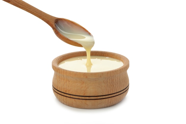 Spoon and bowl with condensed milk isolated on white background