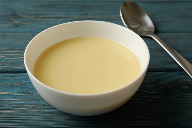 Spoon and bowl with condensed milk on wooden background