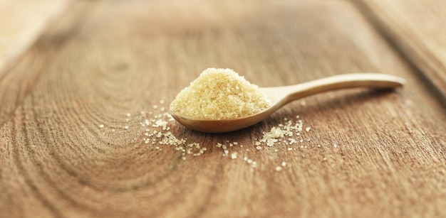 Photo spoon of brown sugar on wooden table against soft blur background selective focus